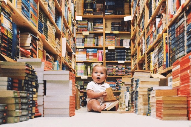 baby zit in een bibliotheek met een stapel boeken voor zich