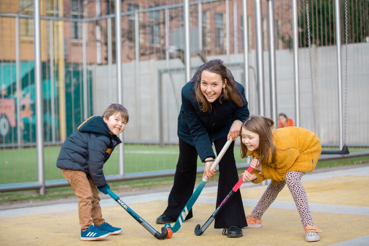 een oppas en twee kinderen die hockey spelen